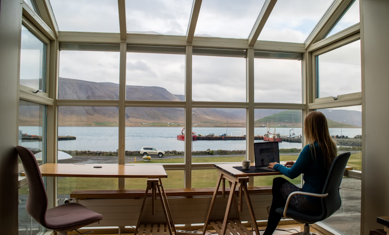 person sitting on chair working on laptop next to big window